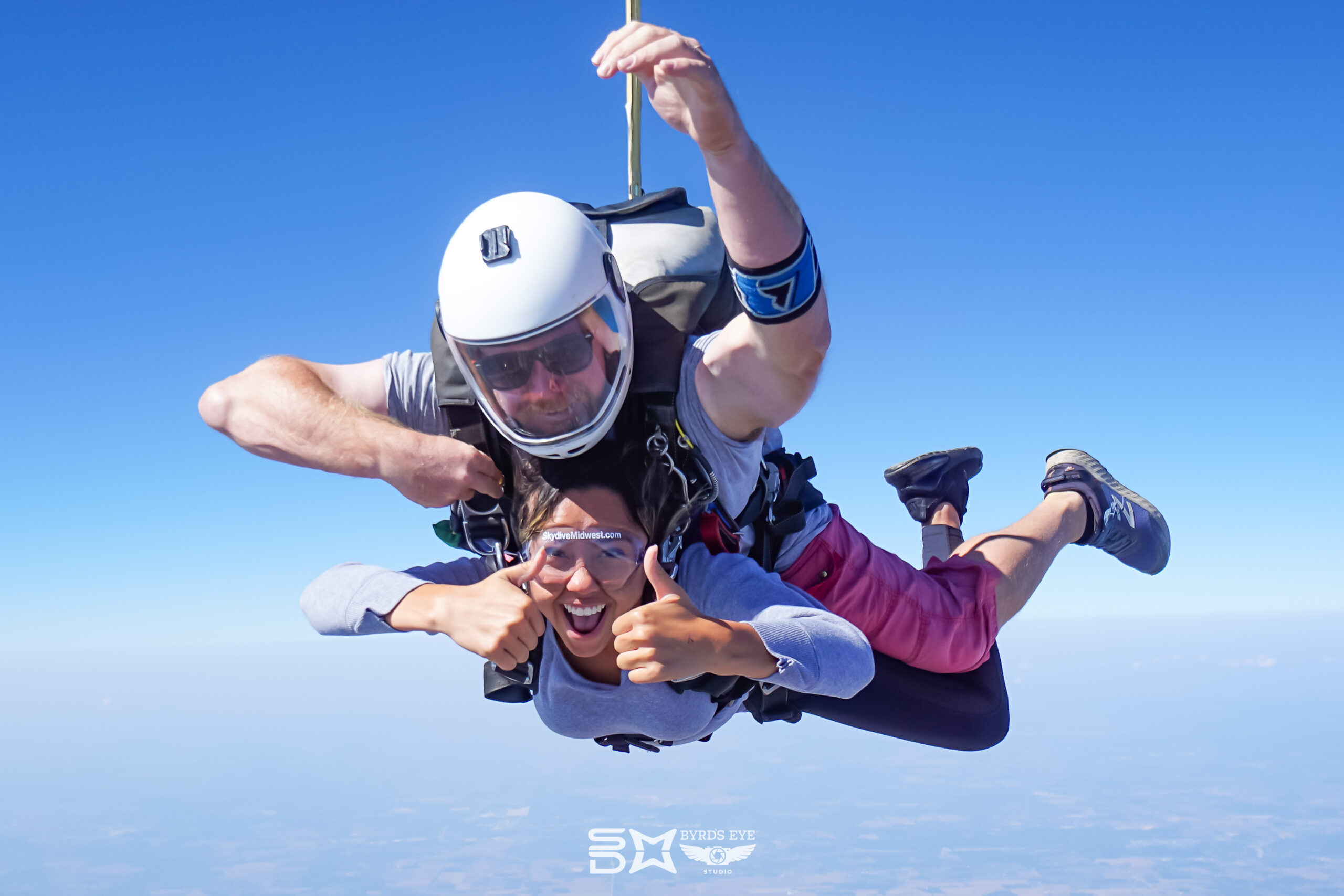 Tandem skydiving student smiling and giving thumbs up to the outside videographer